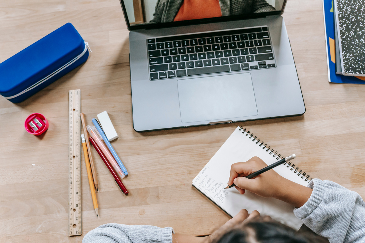 Clever schoolgirl doing homework in notebook while having online lesson