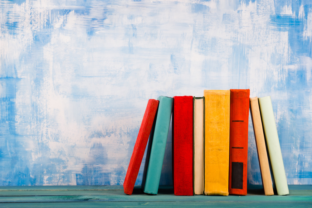 Stack of colorful hardback books, open book on blue background